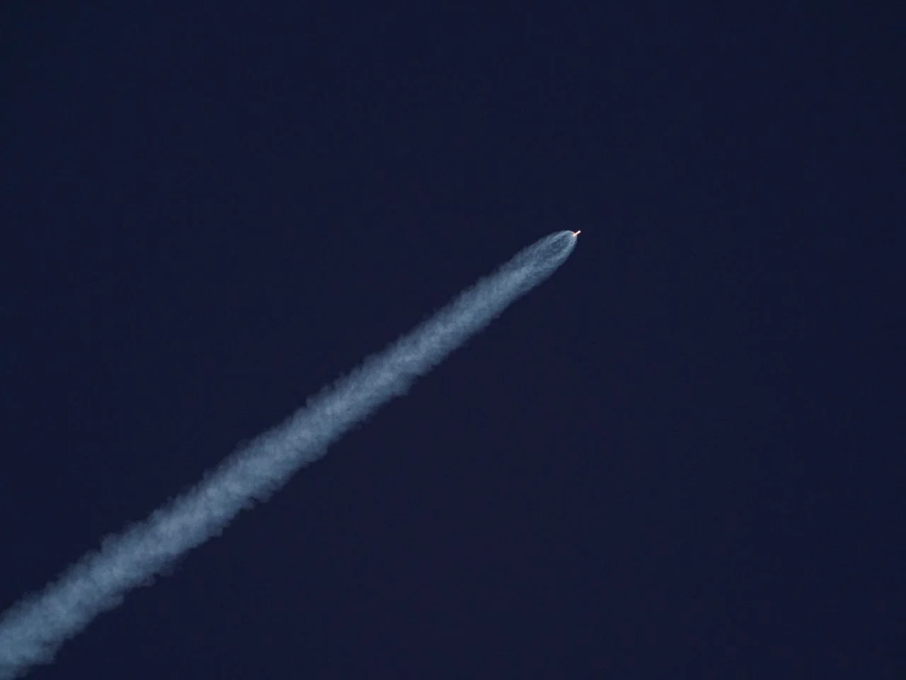 A rocket ascends into the sky, leaving a trail of smoke against the clear blue sky.
